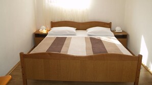 A single bed with a striped bedspread, two bedside tables with lamps, a nightstand with a lamp, and a window with sheer curtains. - Stunning sea View From one Bedroom Apartment Reno (Preko)