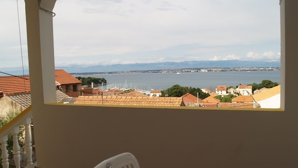 A balcony with a view of a coastal cityscape, including a body of water and distant mountains. - Stunning sea View From one Bedroom Apartment Reno (Preko)