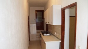 A narrow kitchen with white cabinets, a stove, and a sink. - Stunning sea View From one Bedroom Apartment Reno (Preko)