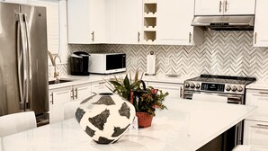 Una cocina moderna con gabinetes blancos, un refrigerador de acero inoxidable, un microondas, una estufa y un recipiente decorativo grande sobre la encimera.