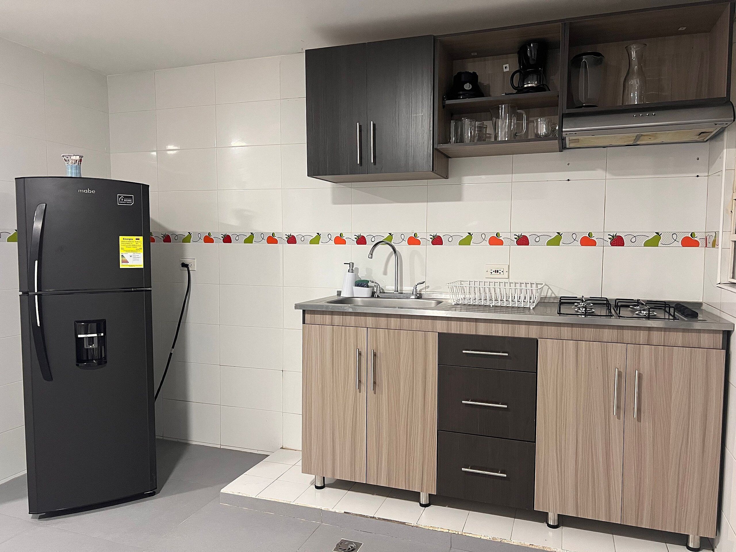 Een keuken met een zwarte koelkast, houten kastjes, een spoelbak en een fornuis.
