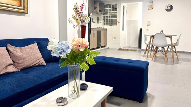 A living room with a blue sofa, a white coffee table, and a vase with flowers. - Apto Super Cómodo al Norte de la Ciudad (Valledupar)