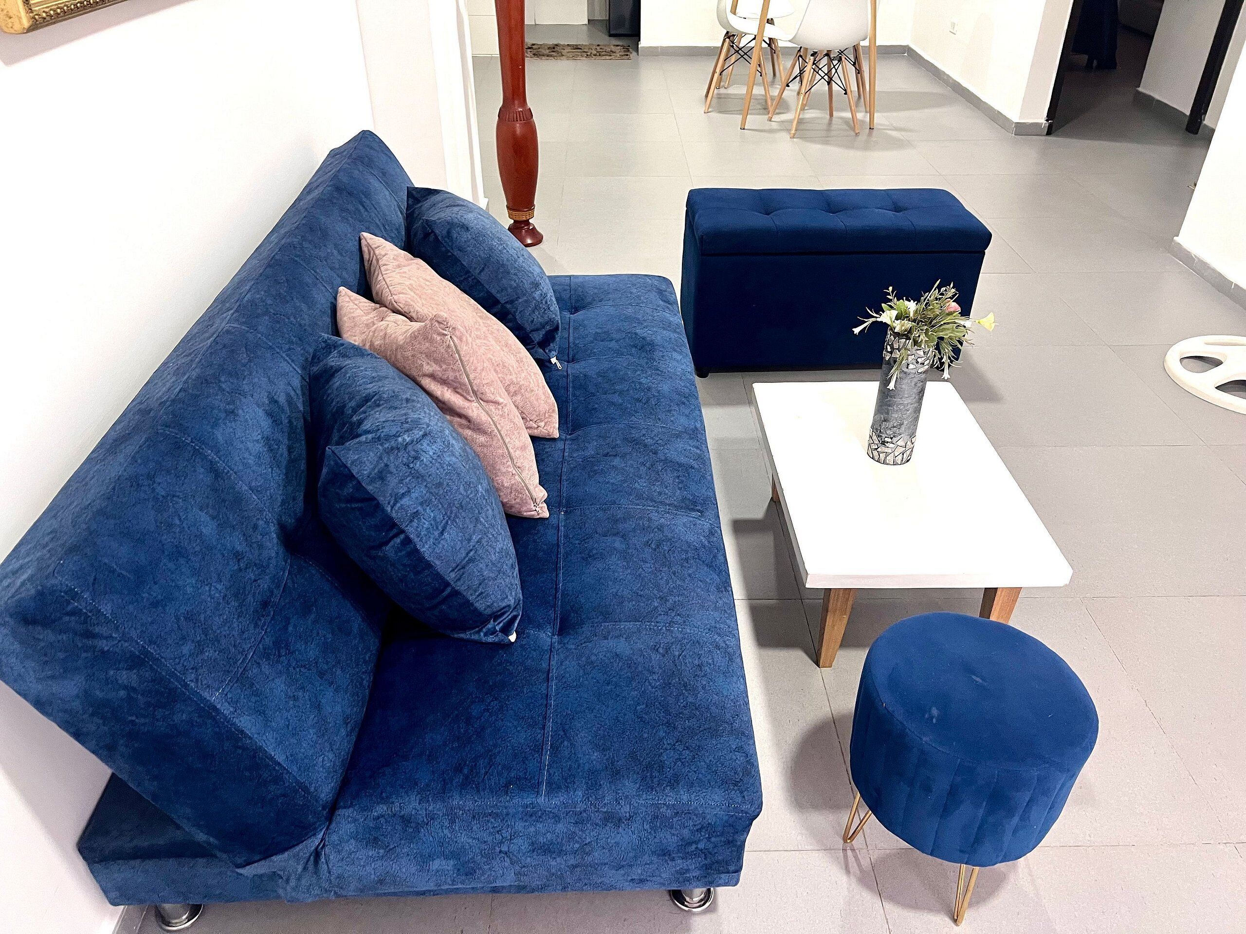 Um sofá azul com otomano combinando e uma pequena mesa branca com um vaso de flores.