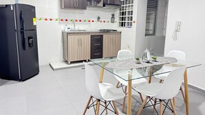 A modern kitchen with a glass dining table, white chairs, and a black refrigerator. - Apto Super Cómodo al Norte de la Ciudad (Valledupar)