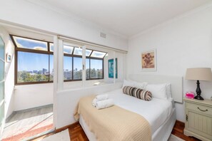 A bedroom with a large bed, a nightstand, a lamp, and a window with a city view.