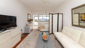 A modern living room with a flat-screen TV, a sofa, a coffee table, and a view of the city through large windows. - Bright and Homey 1 Bedroom in Gardens (Cape Town)