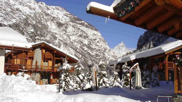 Ein schneebedecktes Berghotel mit Holzhäuschen und blauem Himmel.