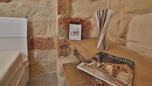 Un mur de pierres apparentes, d’aspect rustique, sur lequel est fixée une étagère en bois, et où sont posés un magazine, un vase et un tableau encadré.