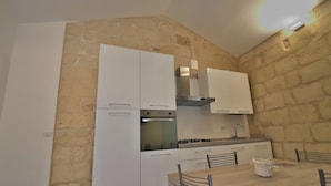 Une cuisine de taille réduite avec des meubles blancs, une cuisinière à gaz et une table à manger avec des chaises.