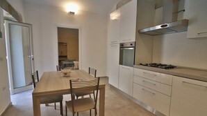 Une cuisine moderne avec des armoires blanches, une hotte en acier inoxydable et un coin repas comprenant une table et des chaises en bois.