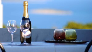 Una botella de champán, dos copas de vino y dos vasos de postre sobre una mesa con una vista panorámica de fondo.