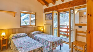 A room with two beds, wooden beams on the ceiling, a window with a mountain view, and a wooden chair. - Apartment La Gran Becca - ID 528 (Antey-Saint-Andre)