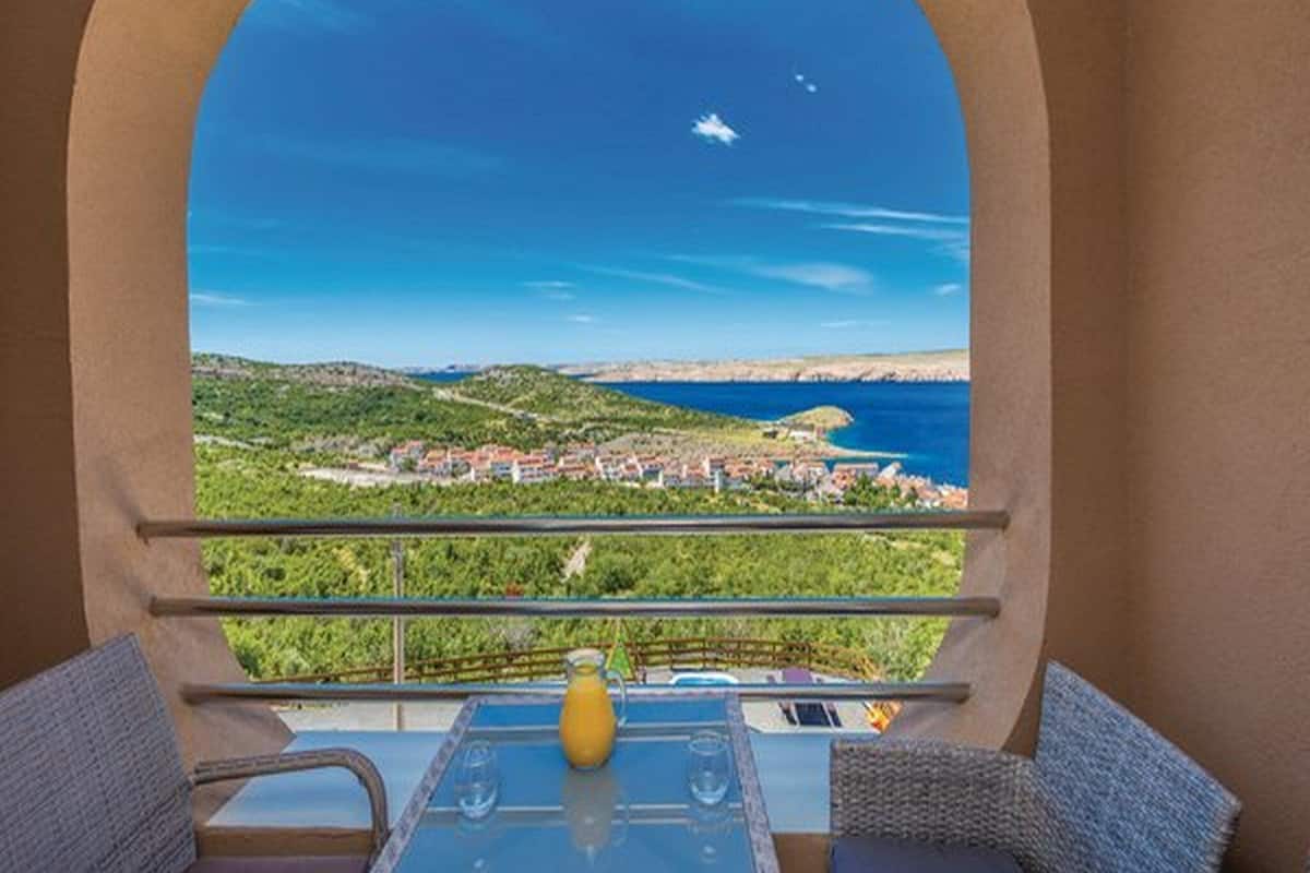A balcony with a clear view of a coastal landscape, including a body of water and a distant town.