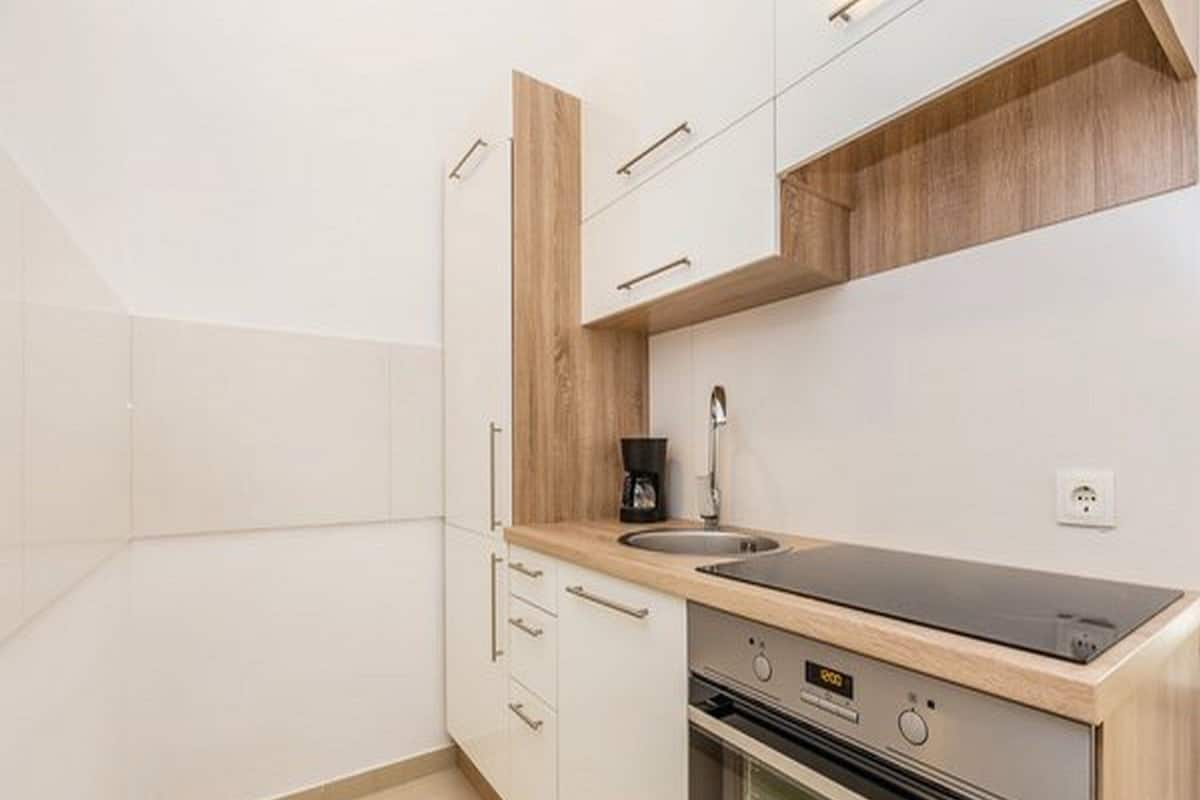 A modern kitchen with white cabinets, a wooden countertop, a built-in oven, and a coffee maker.