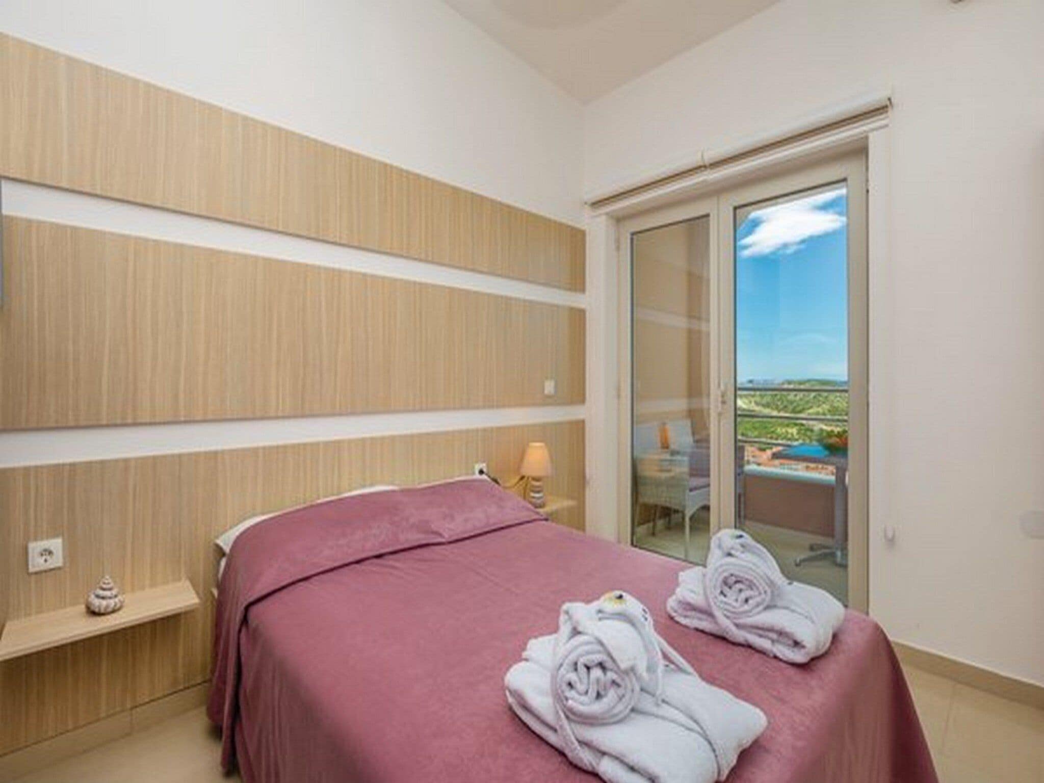 A hotel room with a bed, a small bedside table, a lamp, and a view of a landscape through a glass door.