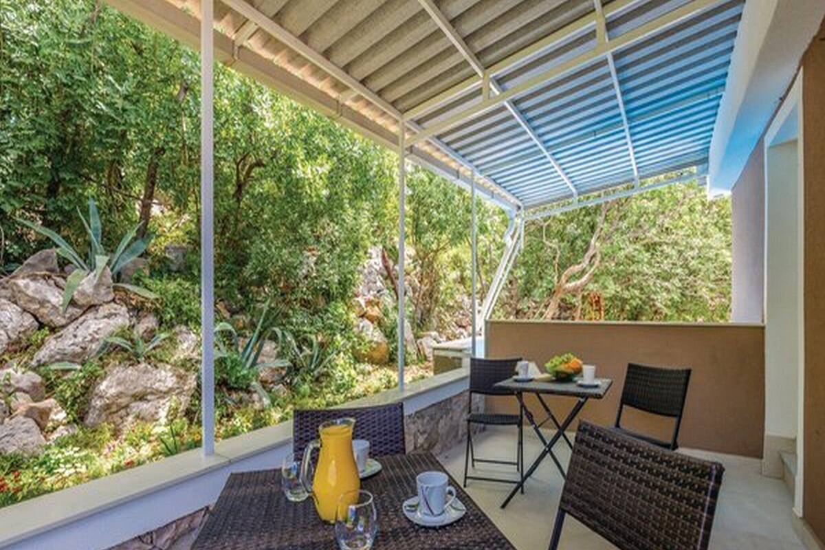An outdoor patio with a table and chairs, surrounded by greenery and rocks.