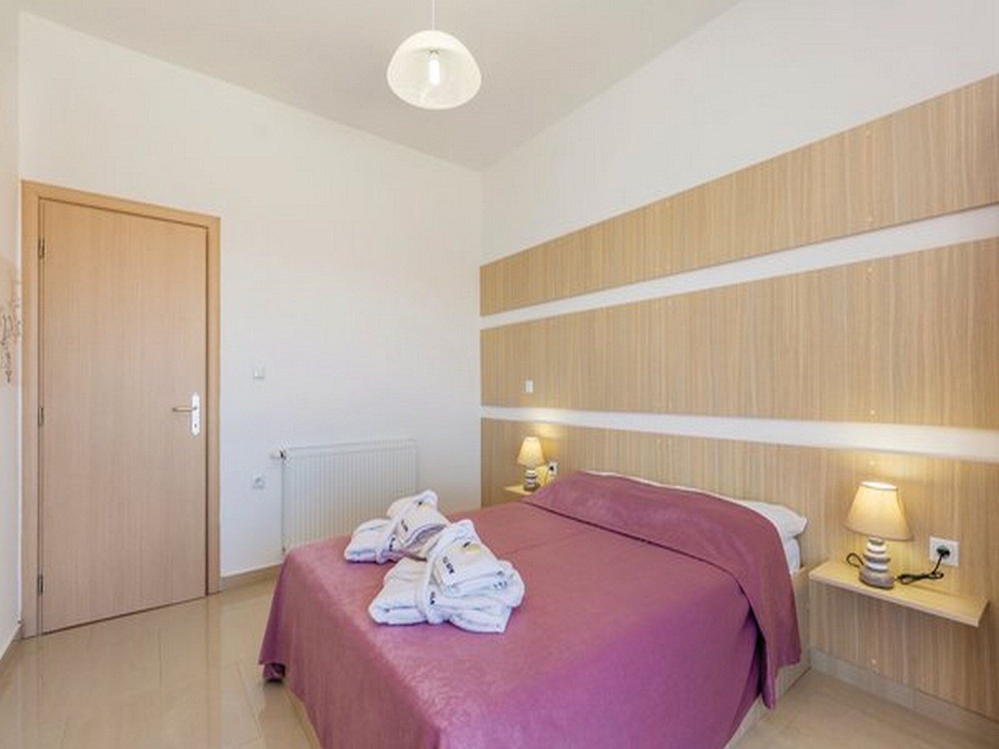 A hotel room with a bed, a wooden headboard, a bedside table with a lamp, and a door.