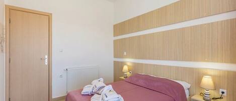 A hotel room with a bed, a wooden headboard, a bedside table with a lamp, and a door.