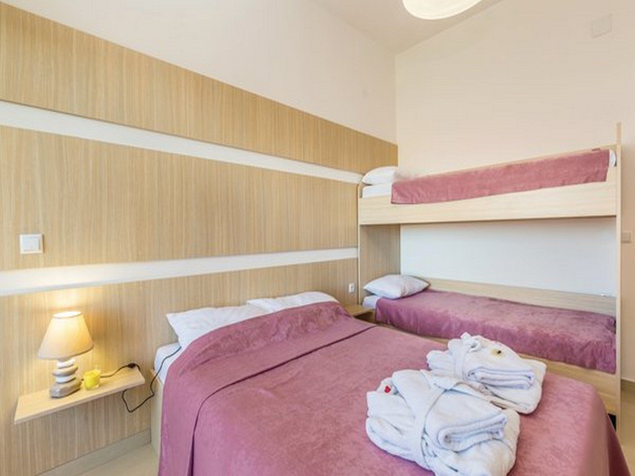 Una camera d'albergo con letti a castello, un comodino con una lampada e un mucchio di asciugamani sul letto.