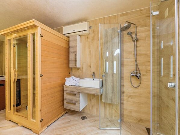 A modern bathroom with a wooden cabinet, a glass shower enclosure, and a sink with a towel. - Apartments Villa Kim (Stinica)