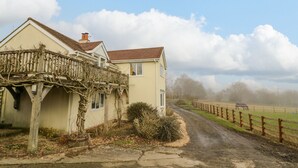 A two-story house with a balcony, a dirt road in front, and a fenced field in the background.