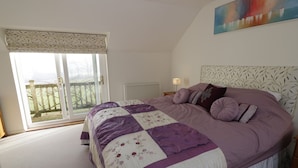 A bedroom with a large bed, a window with a view of a balcony, and a painting on the wall.