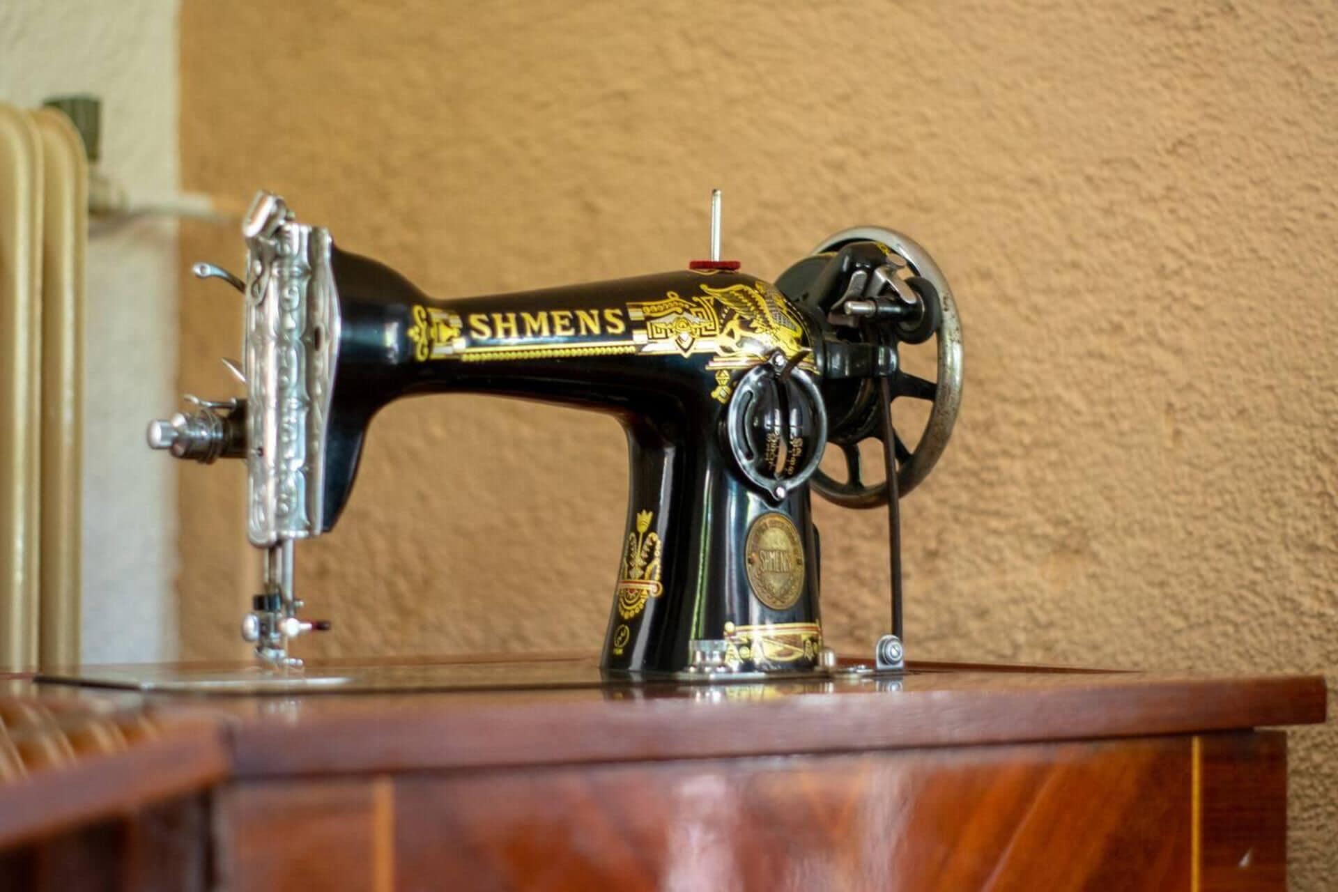 A vintage SHMENS sewing machine with ornate gold detailing, placed on a wooden surface.