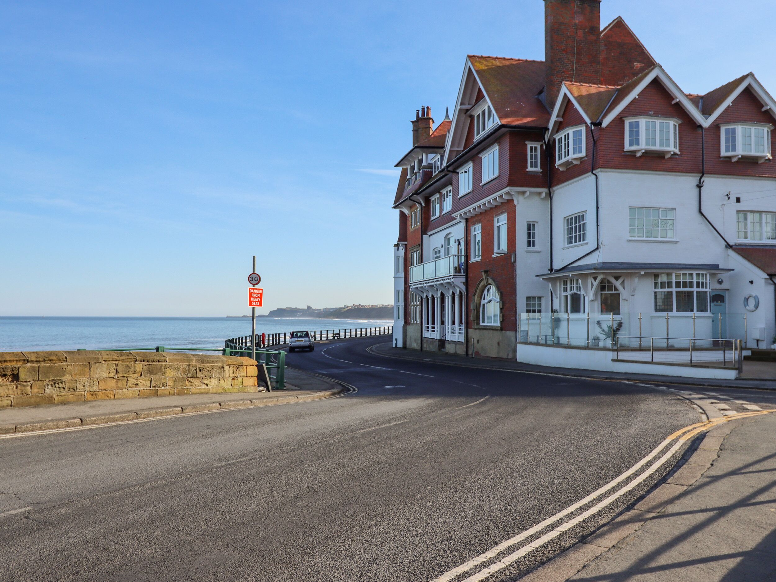 A coastal road with a white building featuring multiple windows and a balcony.