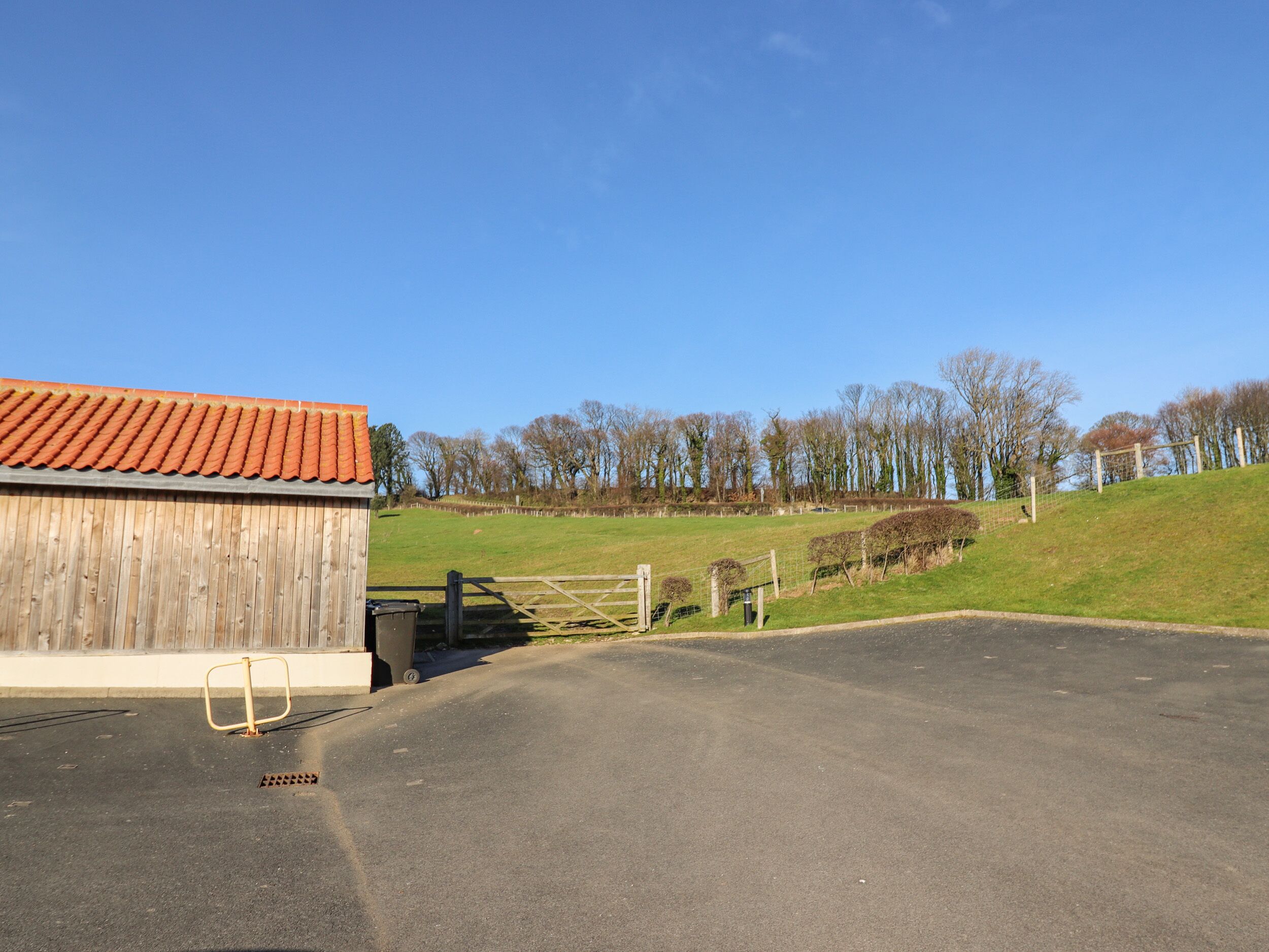 A barn with a red roof, a gated entrance, and a paved driveway leading to a grassy field.