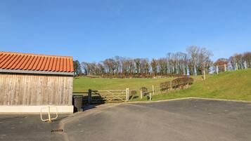 A barn with a red roof, a gated entrance, and a paved driveway leading to a grassy field.