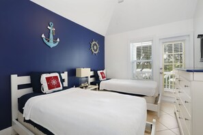 Experience the nautical charm of this cozy retreat, featuring two beds with navy blue headboards and a large window with blinds.