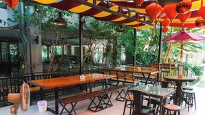 An outdoor cafe with wooden tables and benches, surrounded by greenery. - Pony TopView (Hua Hin)