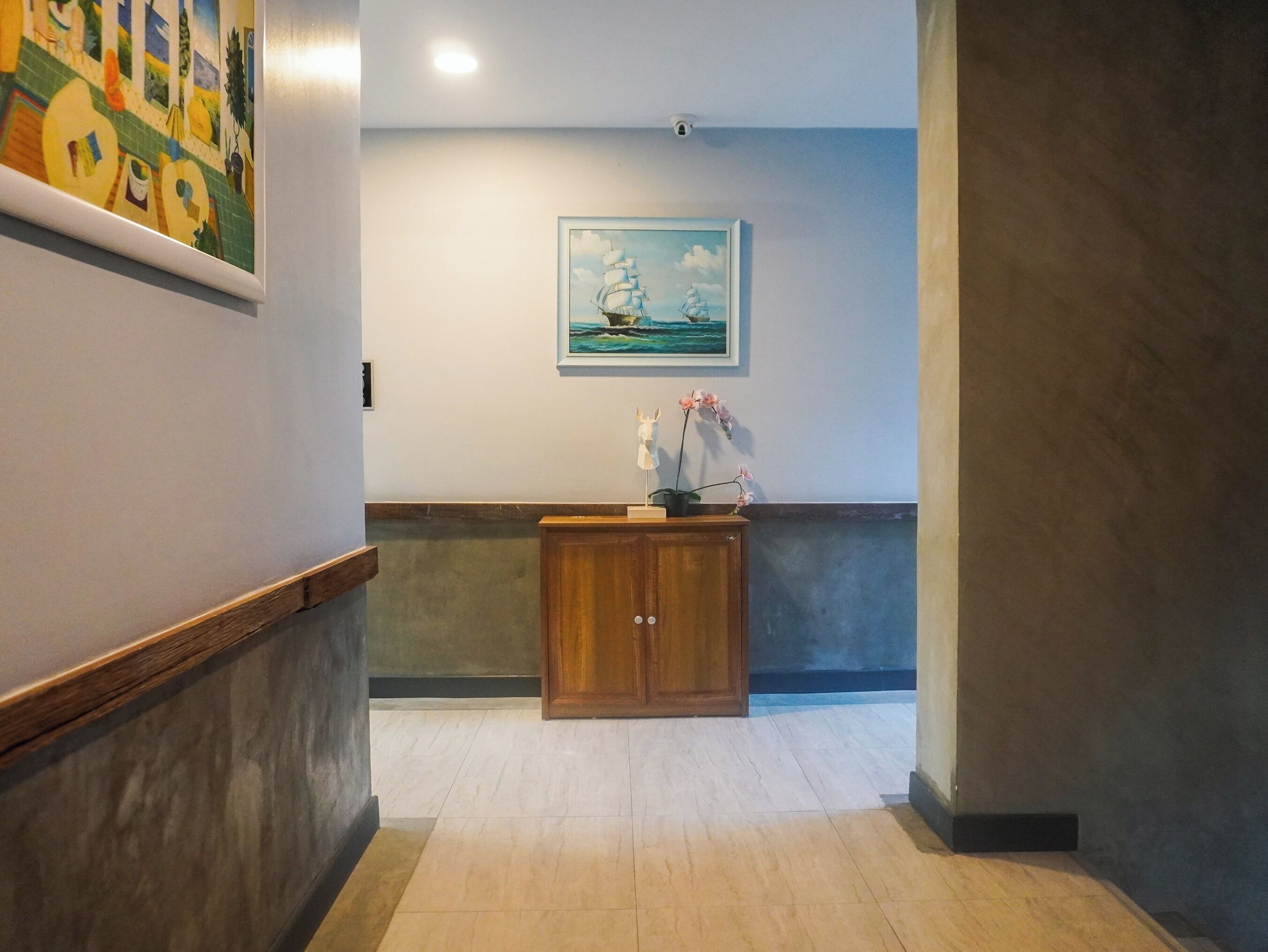 A hallway with a wooden cabinet, a framed painting of a ship, and a security camera on the wall.