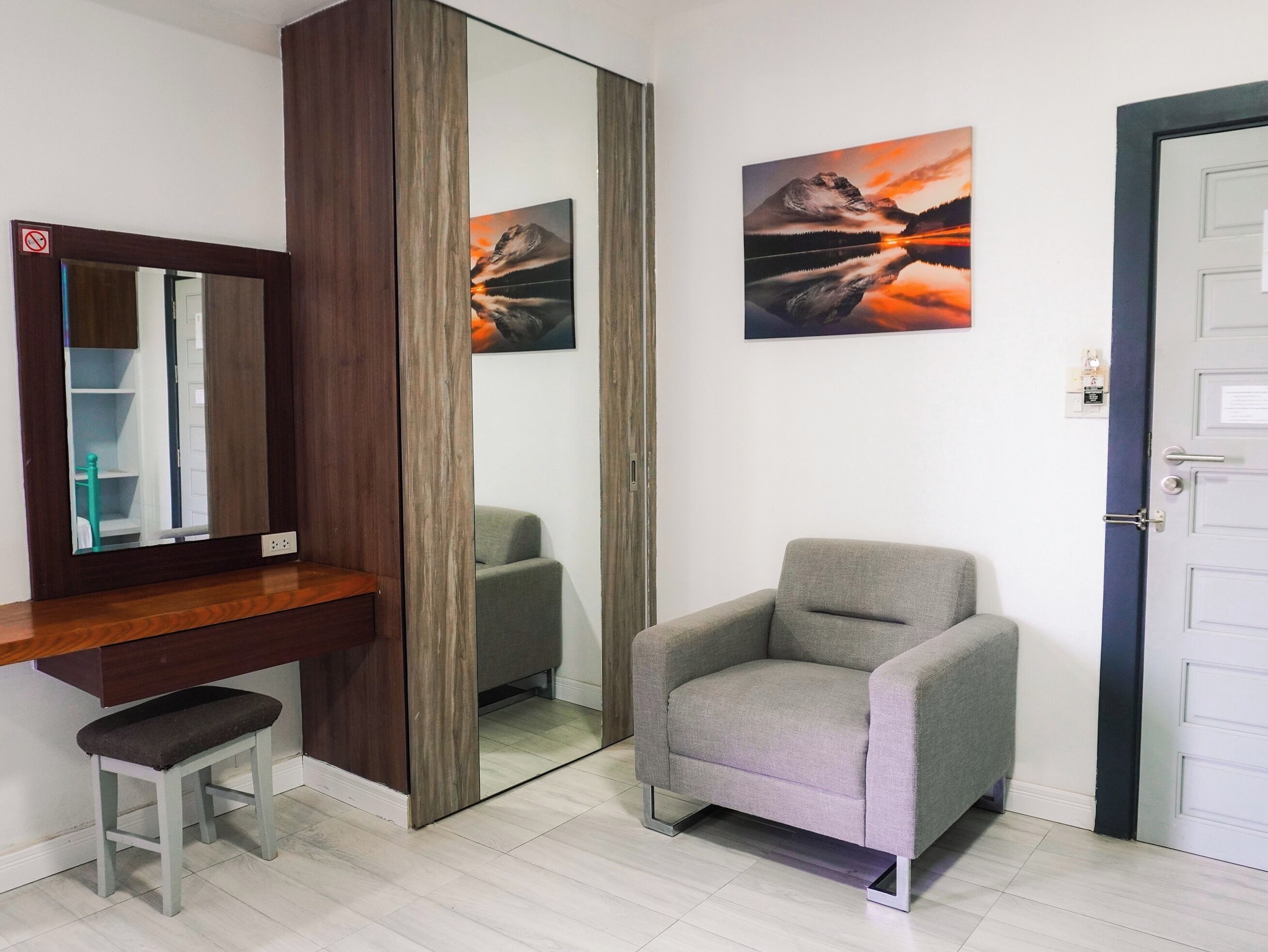 Ein Zimmer mit einem hölzernen Schminktisch, einem Spiegel, einem grauen Sessel und zwei Bildern an der Wand.