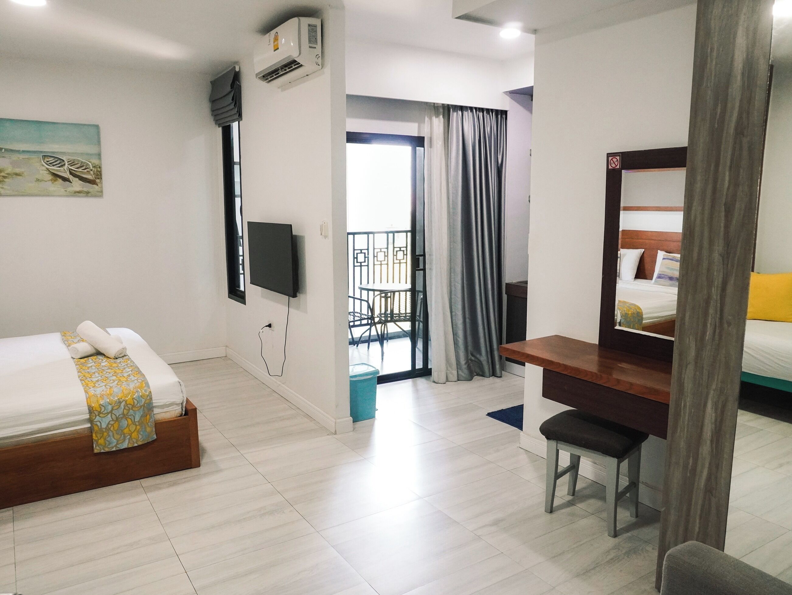 A hotel room with a bed, a desk, a chair, a TV, an air conditioner, and a balcony with a view.