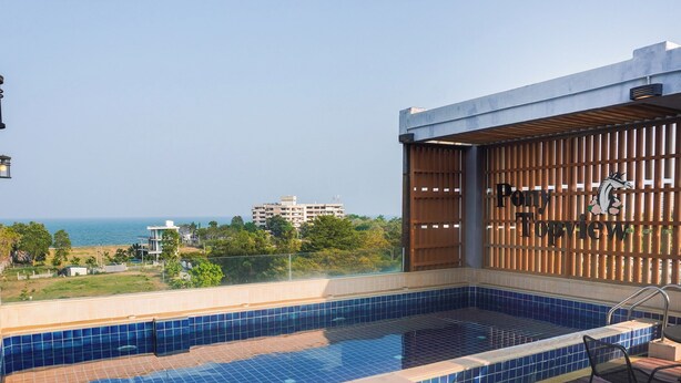 A rooftop pool with blue tiles, wooden deck, lounge chairs, and a view of the ocean and buildings. - Pony TopView (Hua Hin)