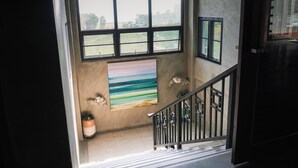 A staircase with a railing, a large window with multiple panes, and a painting on the wall. - Pony TopView (Hua Hin)