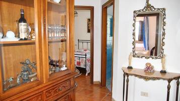 A hallway with a wooden cabinet, a mirror, and a bed in the background.
