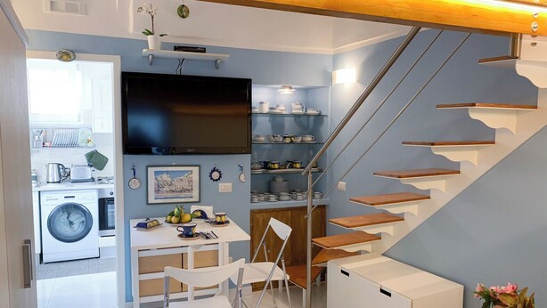 A compact kitchen with a washing machine, a dining area with a table and chairs, and a staircase with wooden steps. - Freeholiday House in Amalfi Coast (Minori)