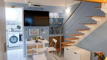 Cocina compacta con lavadora, comedor con mesa y sillas, y escalera con escalones de madera.