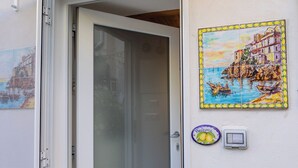 A door with a frosted glass panel, a welcome sign with a lemon design, and a colorful coastal scene painting on the wall. - Freeholiday House in Amalfi Coast (Minori)