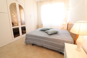 Quarto com cama, almofadas, mesa de cabeceira, luminária, guarda-roupa e espelho.