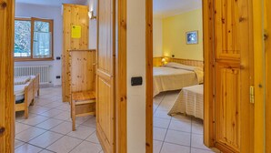 A room with wooden doors, a bed, a chair, and a window with a view of trees. - Apartment La Gran Becca - ID 527 (Antey-Saint-Andre)