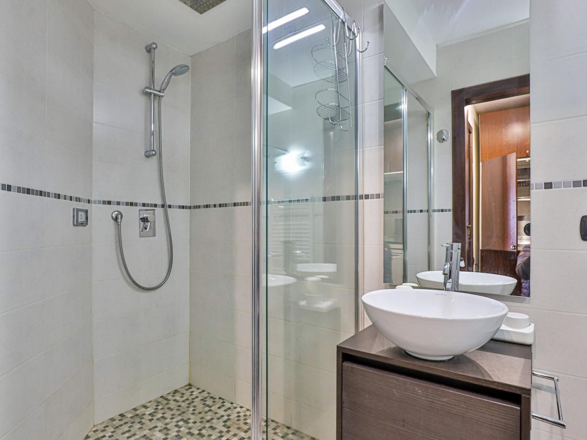 A modern bathroom with a glass-enclosed shower, a large white sink, and a wooden vanity.
