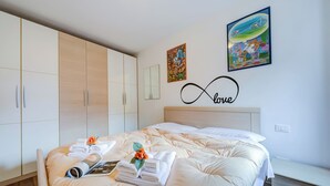 Una cama bien hecha con toallas y una revista, un armario de madera y dos cuadros en la pared.