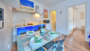 Una cocina moderna con armarios azules, una campana extractora de acero inoxidable y un comedor con mesa de vidrio para cuatro.