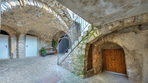 Un patio de paredes de piedra con una puerta de madera, una escalera de metal y una planta en maceta.