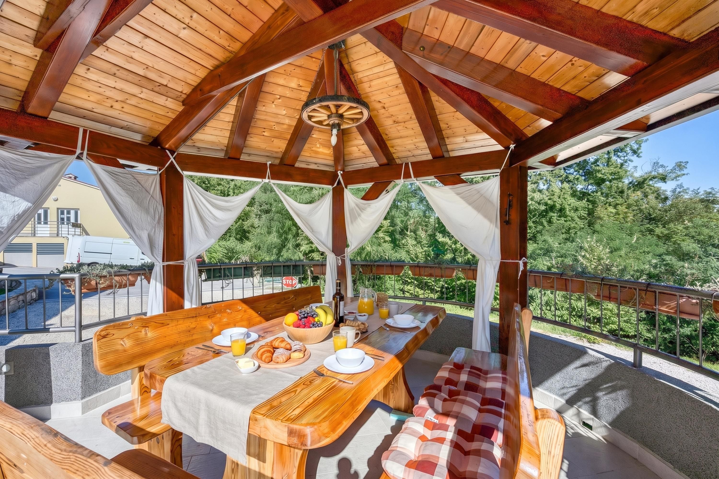 An outdoor wooden pavilion with a table set for breakfast, surrounded by a metal railing.