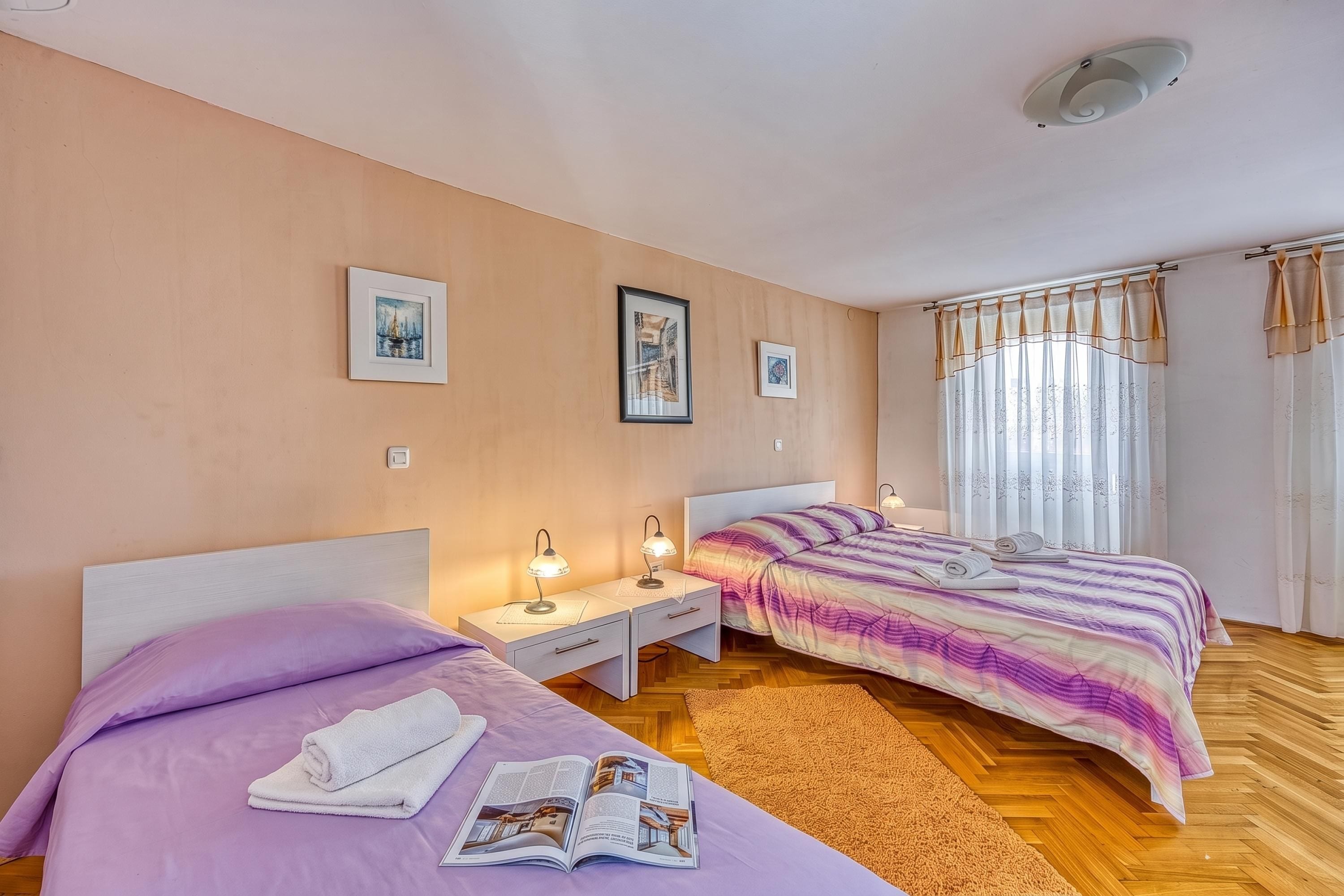 A bedroom with two beds, a nightstand, a lamp, and a window with curtains.
