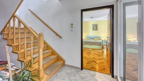 Un escalier en bois mène à une chambre à coucher équipée d’un lit, de tables de chevet et offrant une vue à travers une porte vitrée.